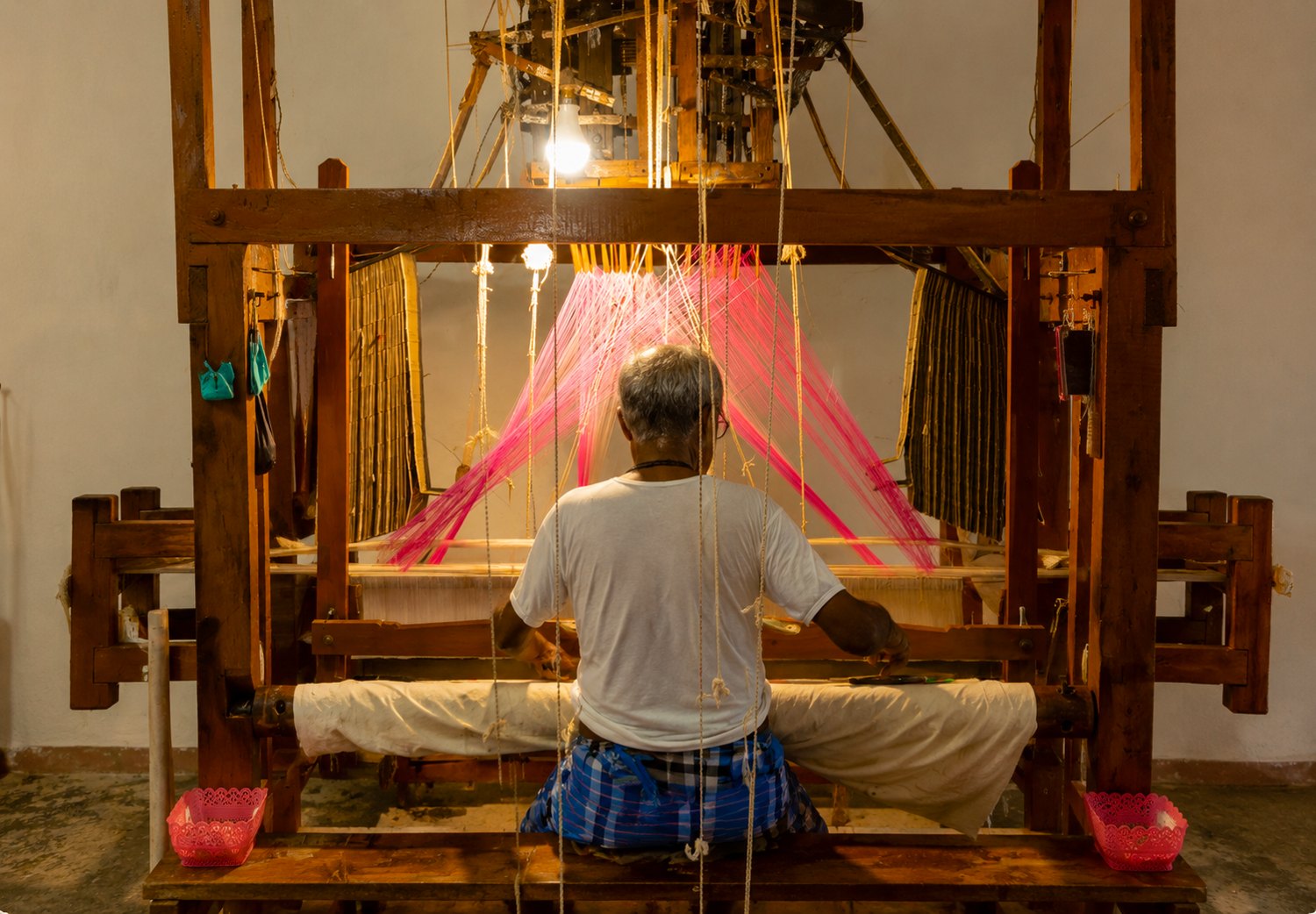 A weaver at a loom with pink threads.